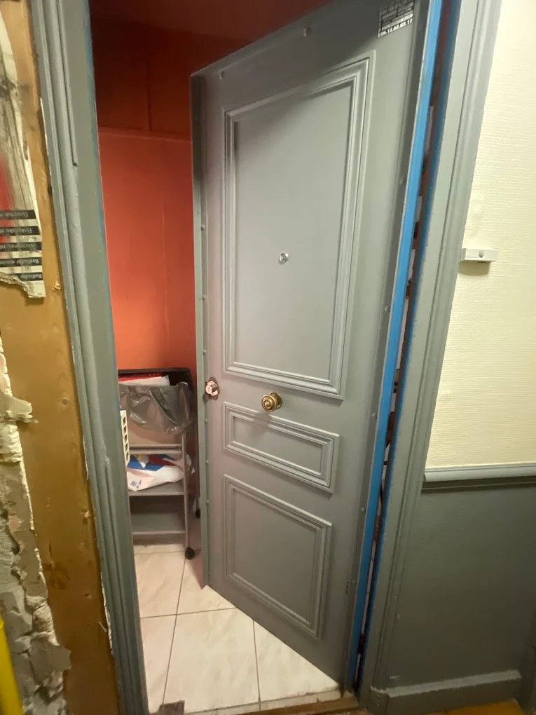 Porte palière grise rénovée à Paris — bouton de tirage laiton, encadrement repeint après intervention